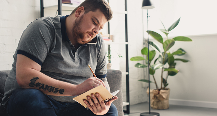 Mand med overvægt sidder i sofa og tager noter