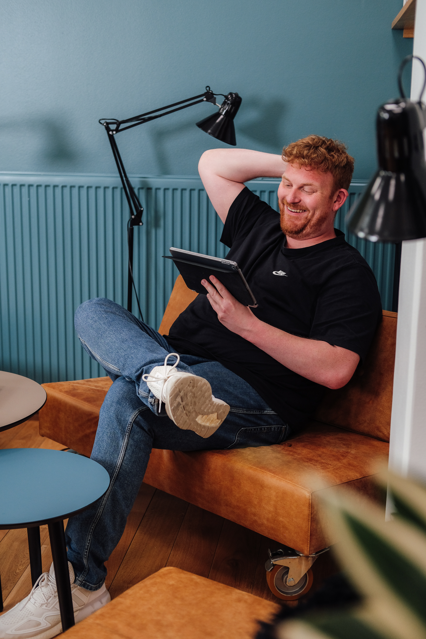 Mand smiler og ser på tablet i sofaen.