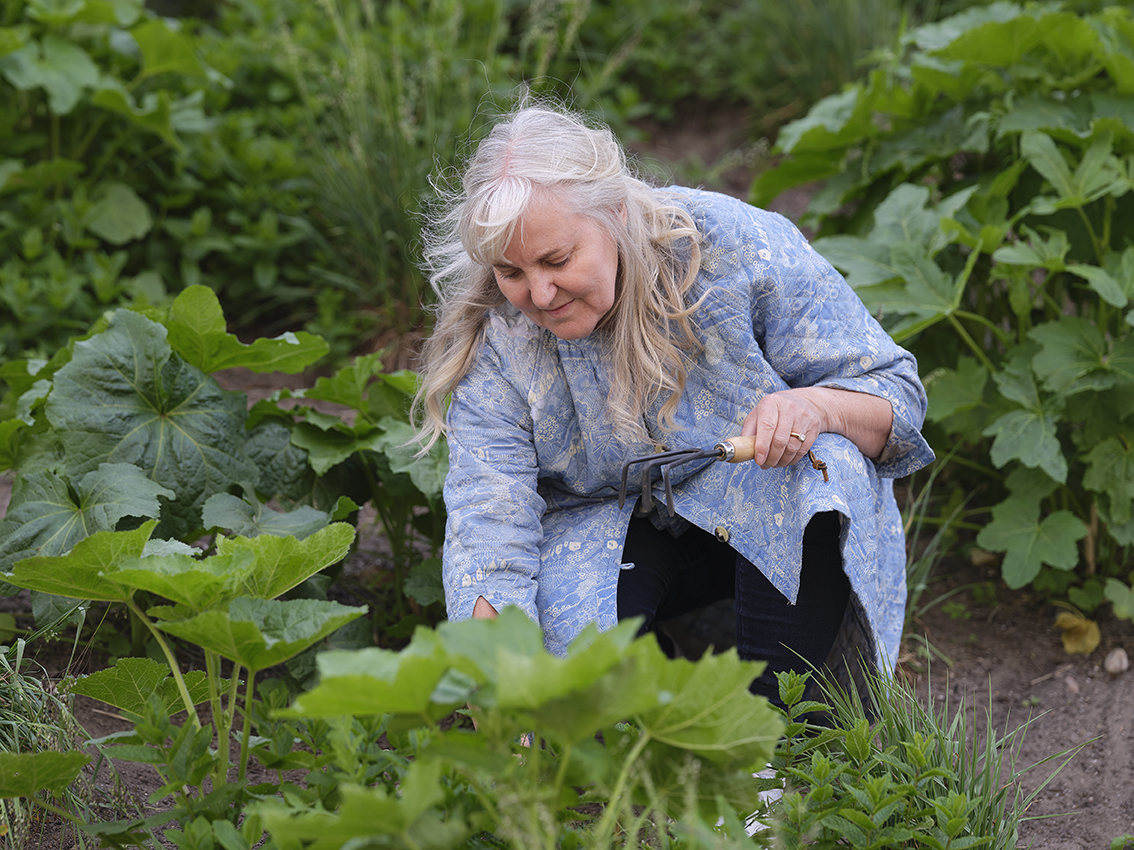 Ældre kvinde rykker ukrudt op i urtehaven.