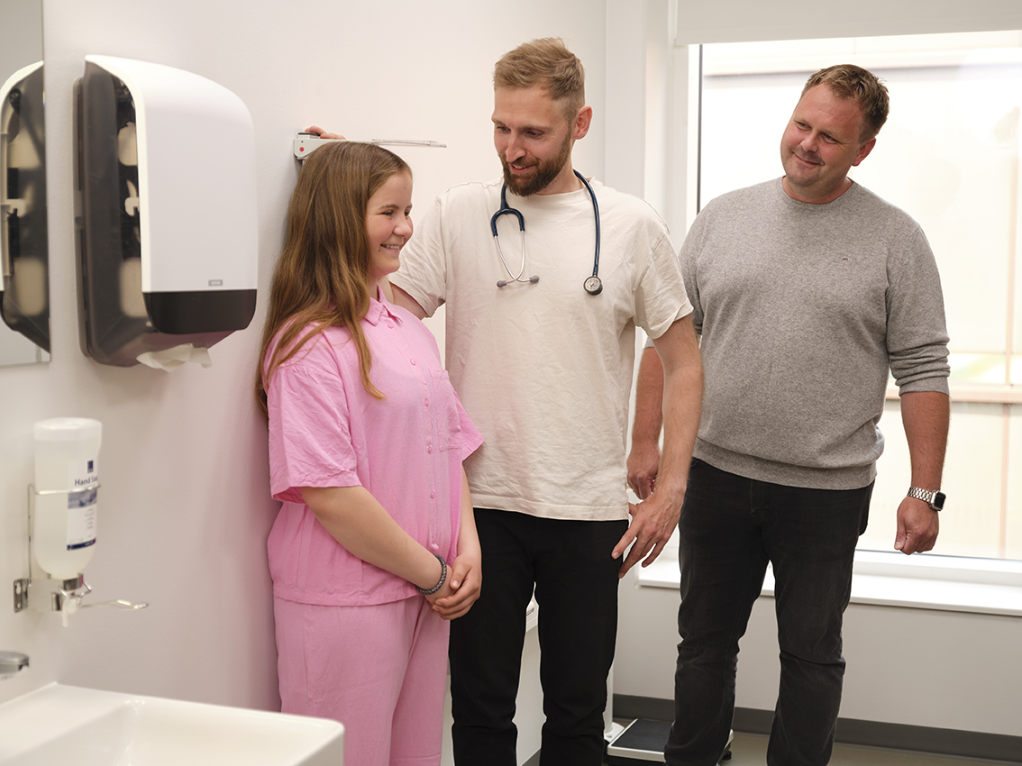 Praktiserende læge måler datters højde, mens far står ved siden af.