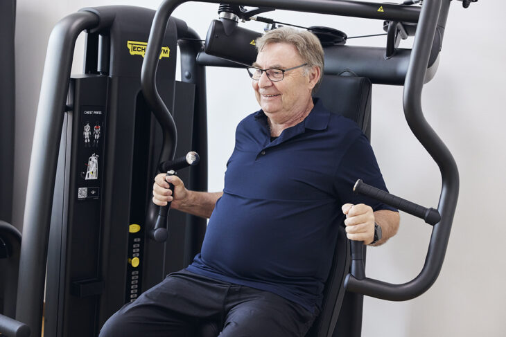 Ældre mand styrketræner overkrop på en maskrine i fitnesscenter.