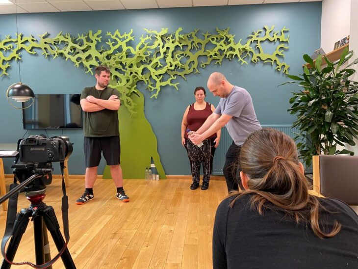 Fysioterapeut viser skånsomme øvelser fra træningsvideoer udviklet til mennesker med svær overvægt.